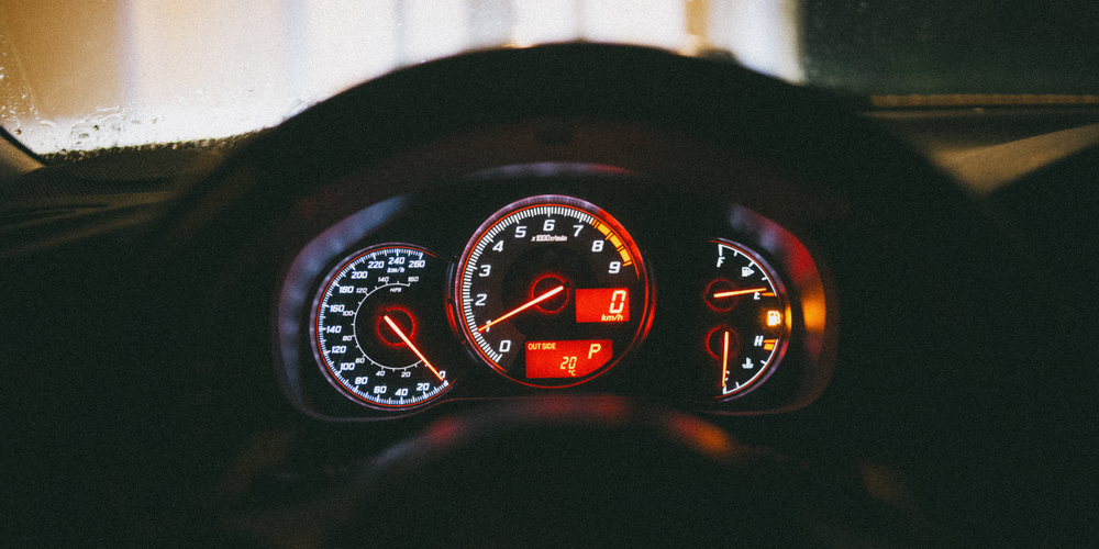 Painel de carro com velocímetro, conta-giros e indicadores iluminados, representando controle, desempenho e monitoramento do veículo durante a condução