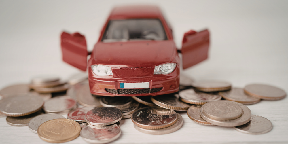 Miniatura de carro sobre moedas representando custo de veículo usado, economia na compra e valorização automotiva