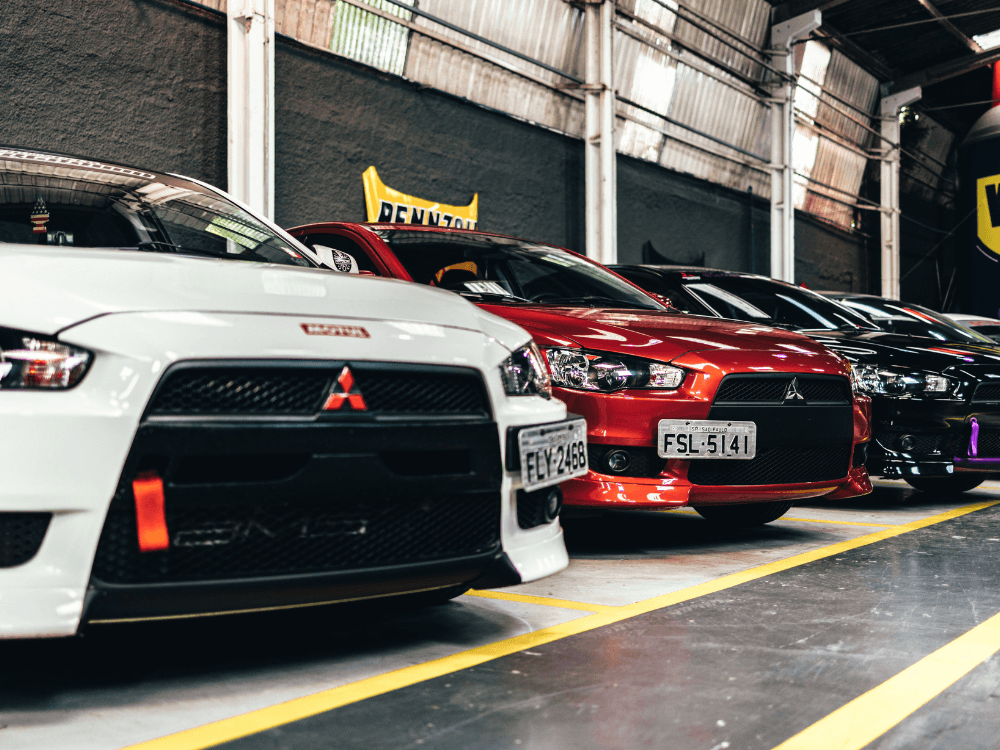 Fileira de automóveis brancos, vermelhos e pretos estacionados no interior de uma loja, ilustrando o mercado de compra e venda de veículos.