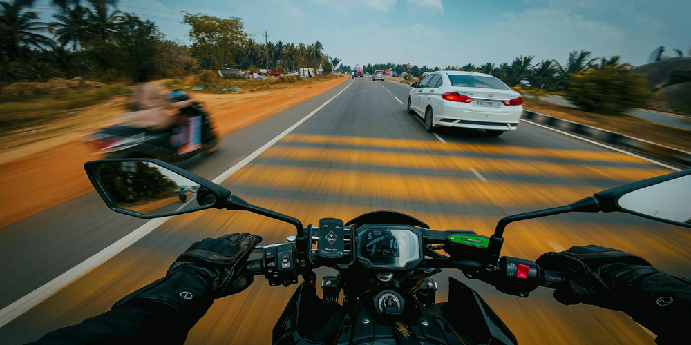Visão de motociclista pilotando em alta velocidade em rodovia ao lado de carros, representando segurança no trânsito, direção em estrada e transporte sobre duas rodas