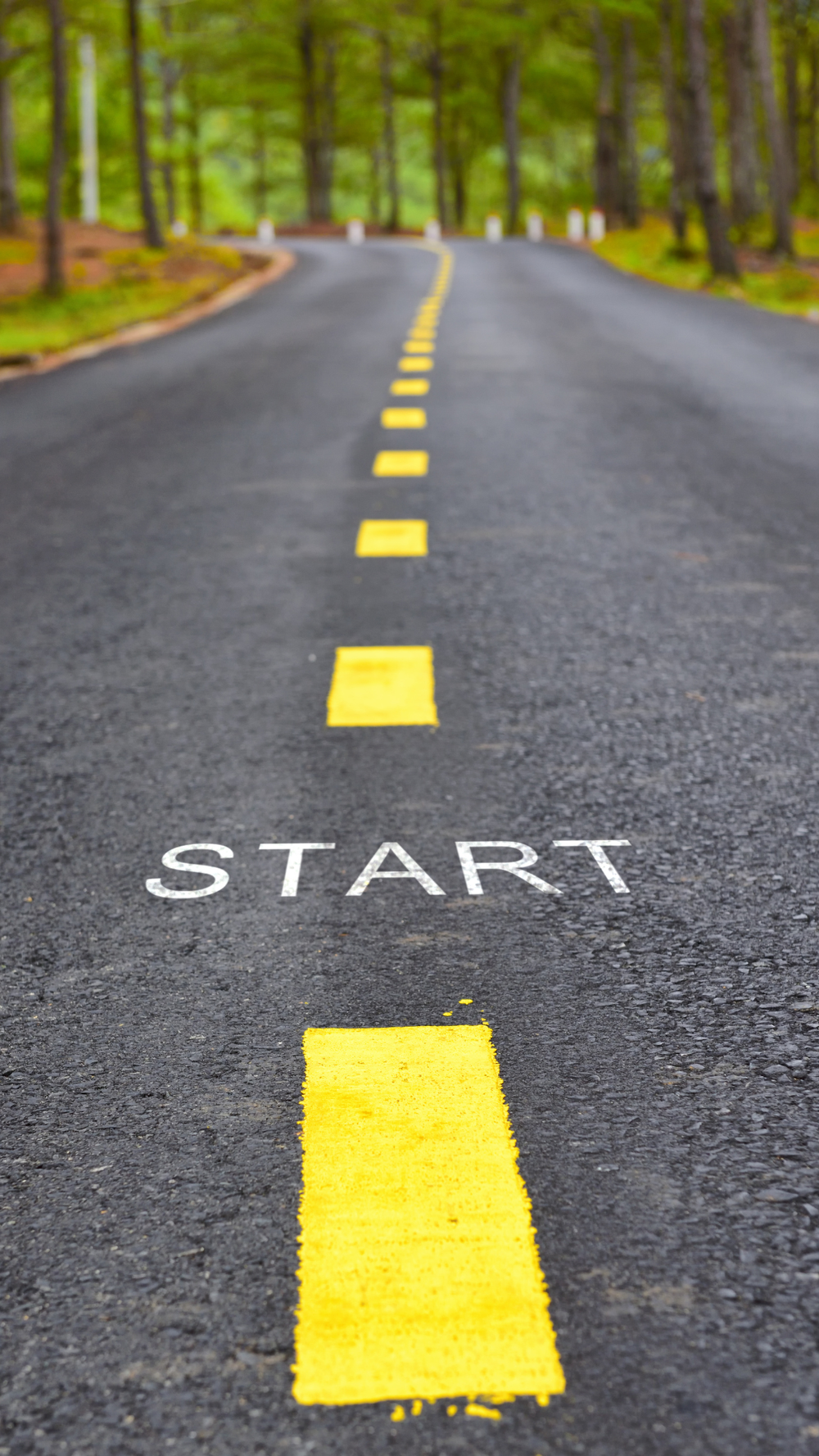 Estrada asfaltada com faixa amarela e a palavra “START” pintada no chão, cercada por árvores, simbolizando início de jornada, novos caminhos e tomada de decisão