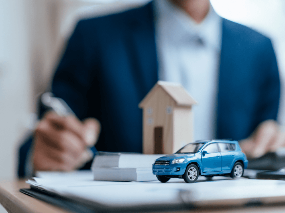 Carro azul em miniatura sobre documentos, com uma pessoa ao fundo, representando a análise antes da compra de um veículo.