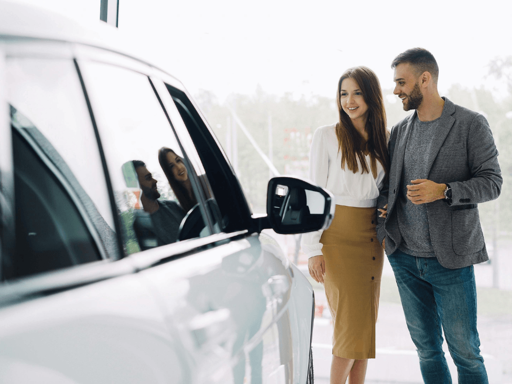 Casal sorrindo enquanto olha para seu novo carro