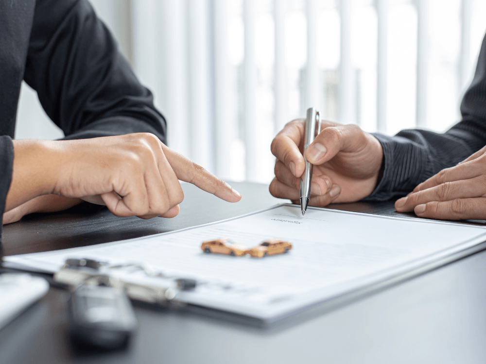 Duas pessoas analisando e assinando documentos sobre uma mesa durante uma negociação relacionada à compra de um veículo.