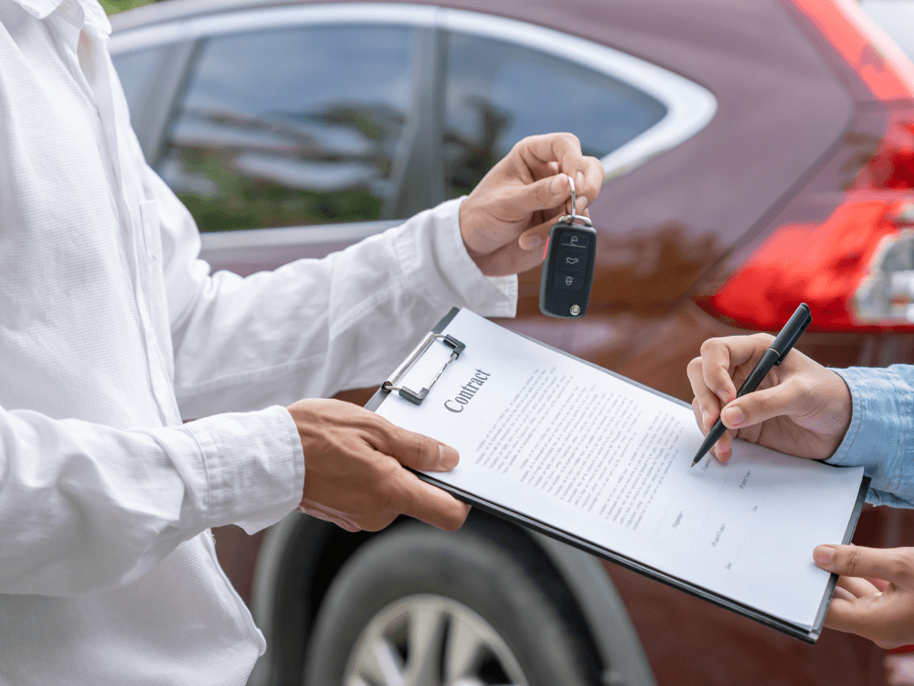 Pessoa assinando contrato e recendo a chave do carro da mão de um vendedor