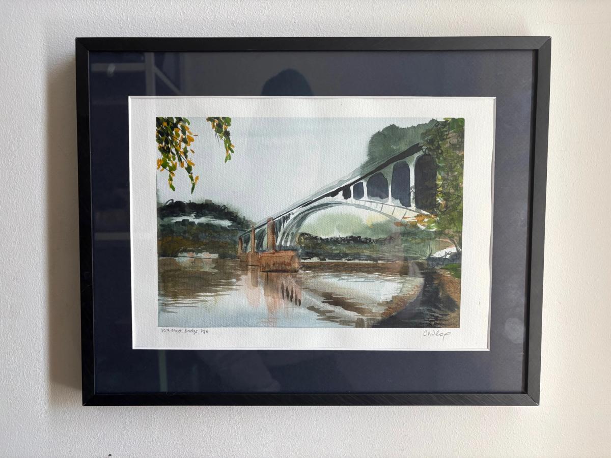 Original watercolor painting of the 40th Street Bridge and its reflection in the Allegheny River, framed in black with a midnight blue matte and hung on a wall