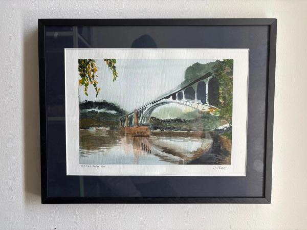 Original watercolor painting of the 40th Street Bridge and its reflection in the Allegheny River, framed in black with a midnight blue matte and hung on a wall