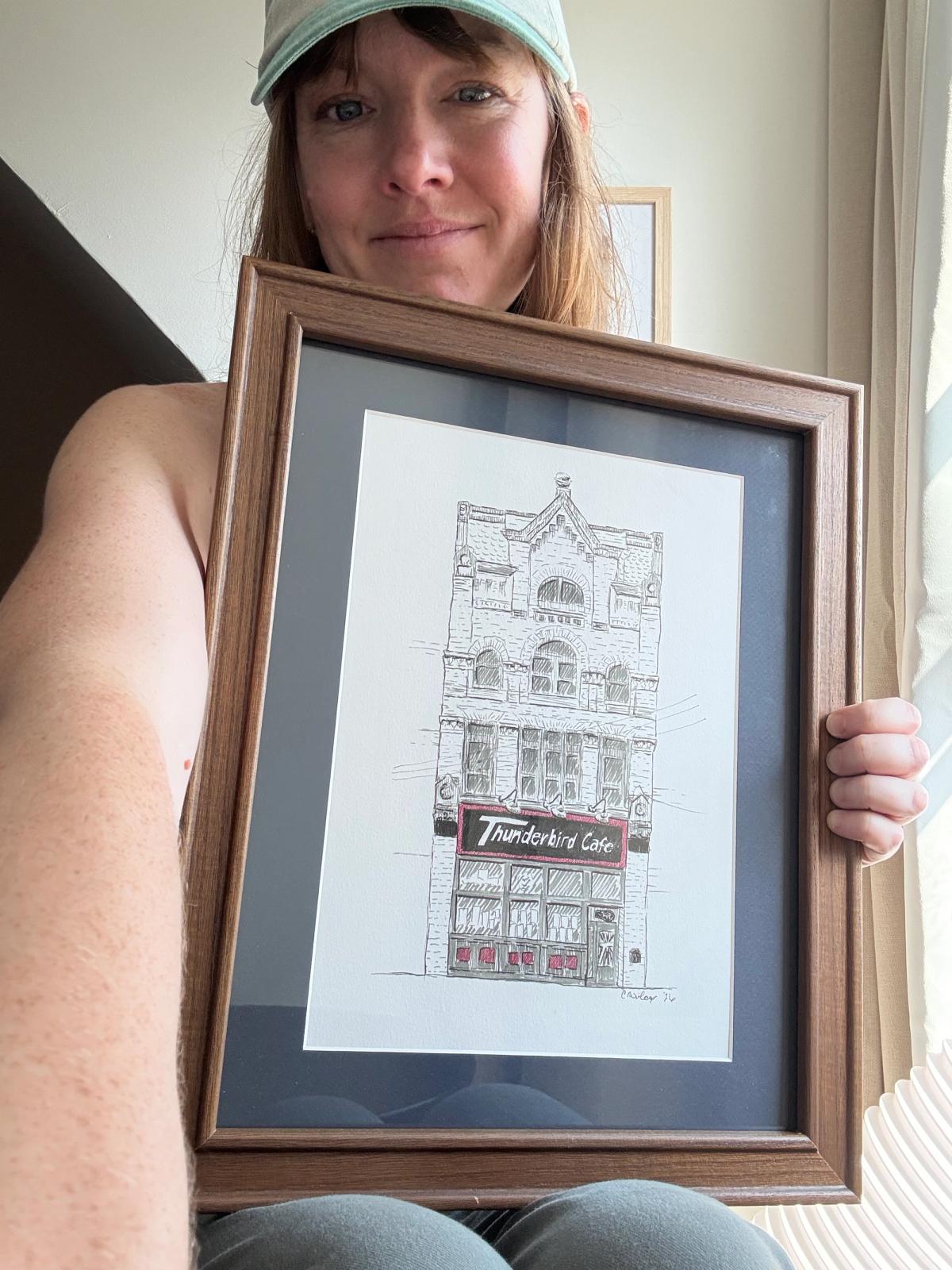 Artist holding framed original artwork of Thunderbird Cafe and Music Hall in 11x14 wooden frame