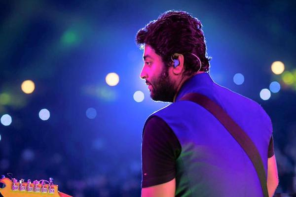 Arijit Singh performing live on stage under blue and purple concert lighting
