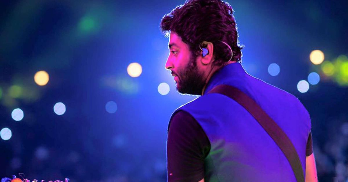 Arijit Singh performing live on stage under blue and purple concert lighting