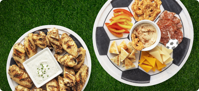 Grilled chicken wings on a soccer ball styled plate and snacks and dip on another soccer ball styled plate