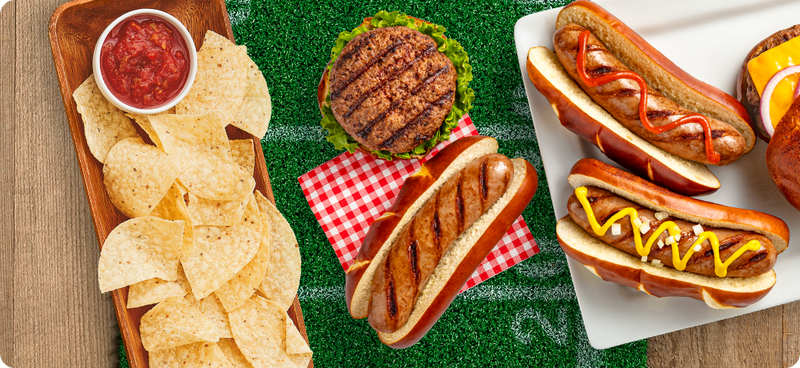 Tortilla chips, salsa, brats and hamburgers plated on top of a football field and wood surface
