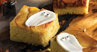 Square slices of citrus upside-down cake decorated with white icing ghosts with candy eyes for Halloween, served on a wooden board.