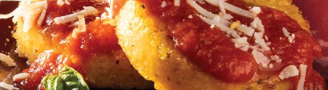 Two round pan-fried polenta cakes topped with red tomato sauce, shredded cheese, and fresh basil on a dark red plate.