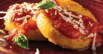 Two round pan-fried polenta cakes topped with red tomato sauce, shredded cheese, and fresh basil on a dark red plate.