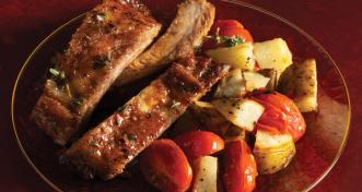 Glazed pork ribs served with roasted potato wedges and cherry tomatoes on a clear red glass plate.