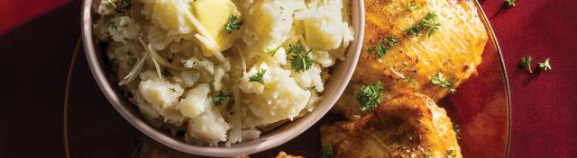 A dinner plate featuring glazed roasted chicken thighs served alongside a bowl of mashed potatoes garnished with butter, shredded cheese, and chopped parsley.