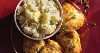 A dinner plate featuring glazed roasted chicken thighs served alongside a bowl of mashed potatoes garnished with butter, shredded cheese, and chopped parsley.