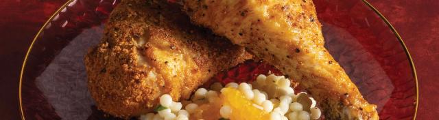 Two crispy breaded baked chicken drumsticks served over a bed of pearled couscous mixed with mandarin orange segments on a glass plate.