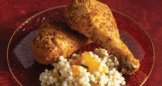 Two crispy breaded baked chicken drumsticks served over a bed of pearled couscous mixed with mandarin orange segments on a glass plate.