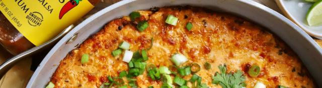 A baked cheesy dip in a round skillet topped with chopped green onions and cilantro, served with fresh lime wedges.