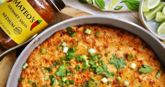 A baked cheesy dip in a round skillet topped with chopped green onions and cilantro, served with fresh lime wedges.