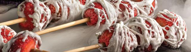 Strawberry skewers wrapped in marshmallow web icing for a Halloween theme, surrounded by white fog.