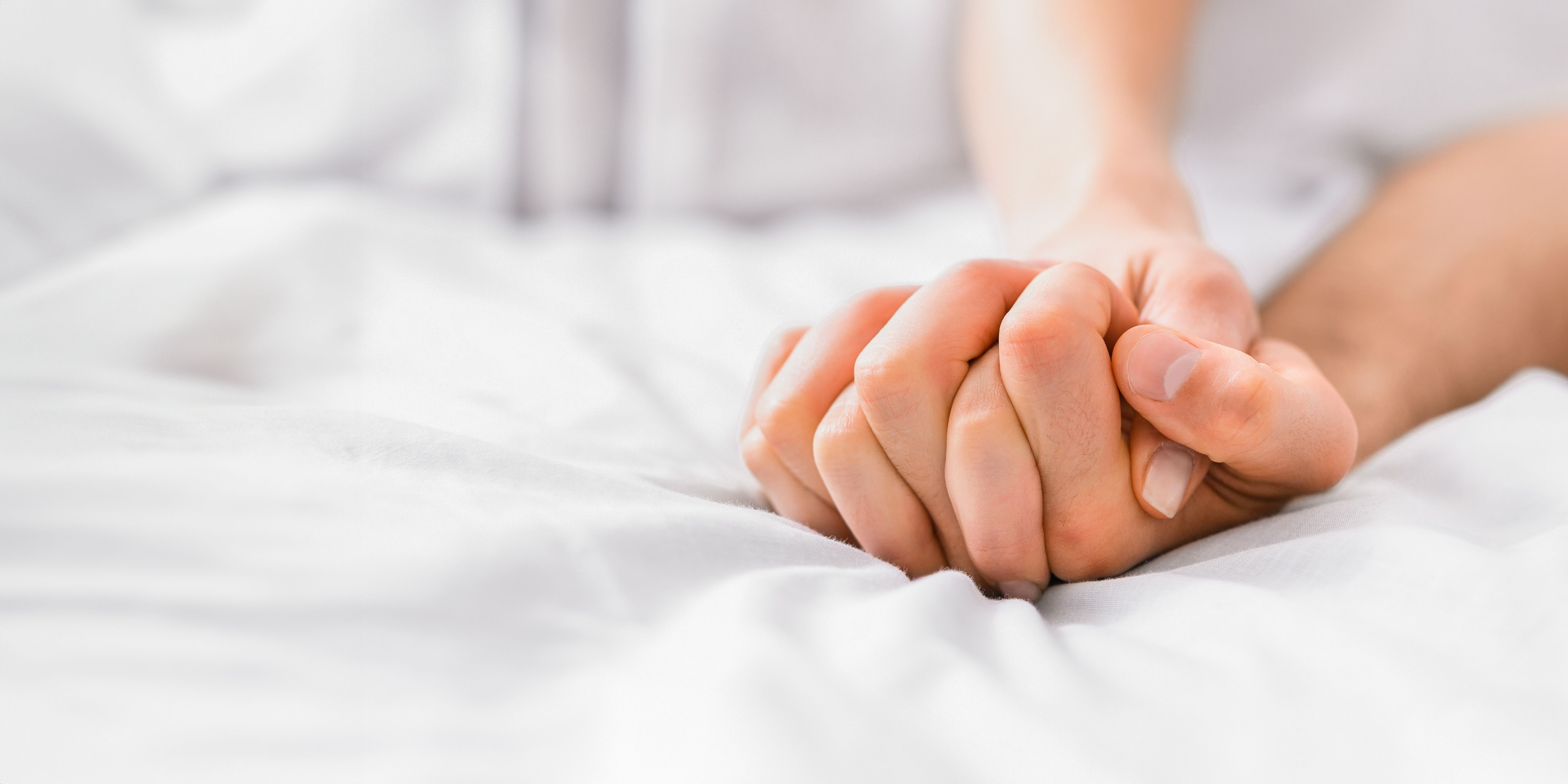 A close-up shot of two hands intertwined on a white bed