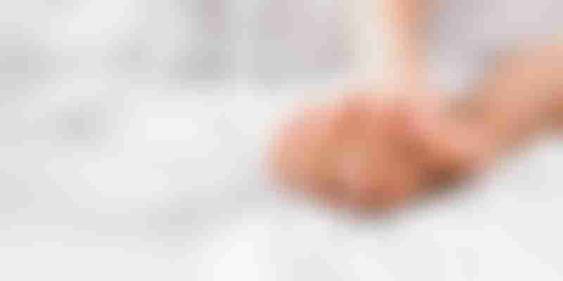 A close-up shot of two hands intertwined on a white bed