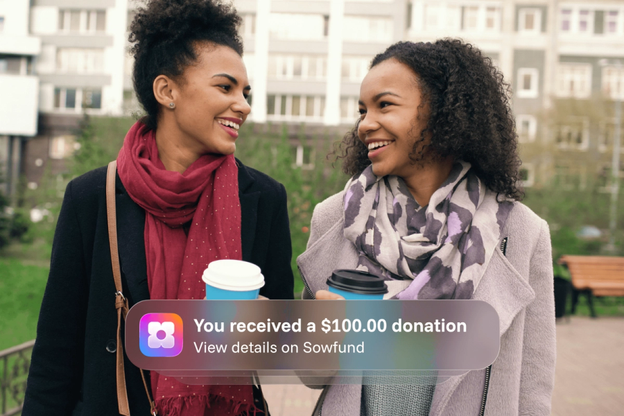 Two women smiling at each other while walking outdoors with coffee cups, overlaid with a Sowfund app notification: "You received a $100.00 donation — View details on Sowfund.