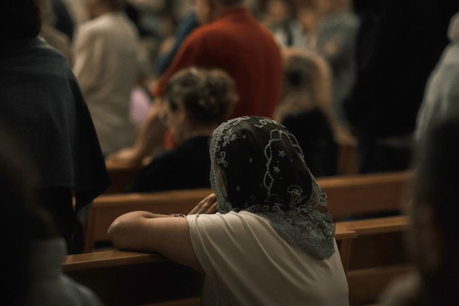 Image 1: A woman wearing an embroidered lace head covering seated in a church pew, surrounded by a congregation in the background.