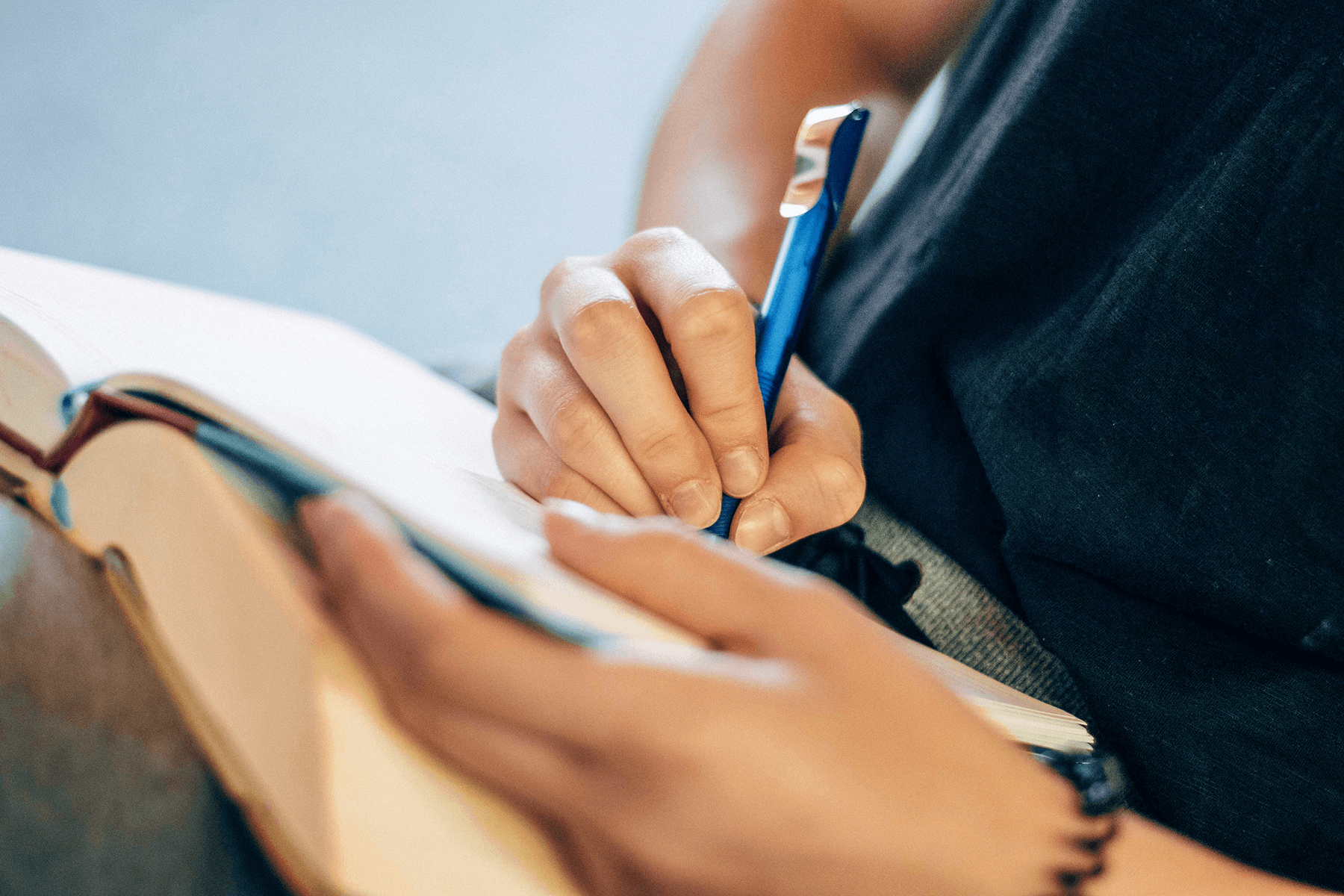 A close-up of a person's hands writing in a notebook with a blue pen.