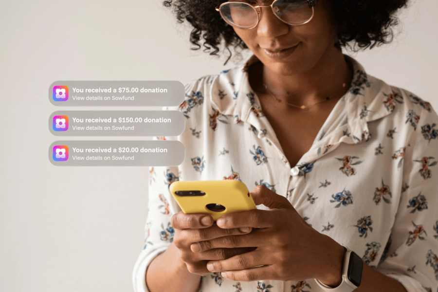 A woman with glasses looking at her yellow phone, with three Sowfund donation notifications showing received amounts of $75.00, $150.00, and $20.00.