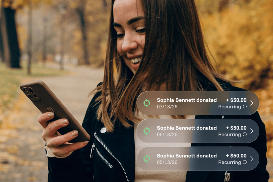 A woman smiling at her phone outdoors in an autumn setting, with three Sowfund recurring donation notifications showing Sophia Bennett's monthly $50.00 contributions on 05/13/26, 06/13/26, and 07/13/26.