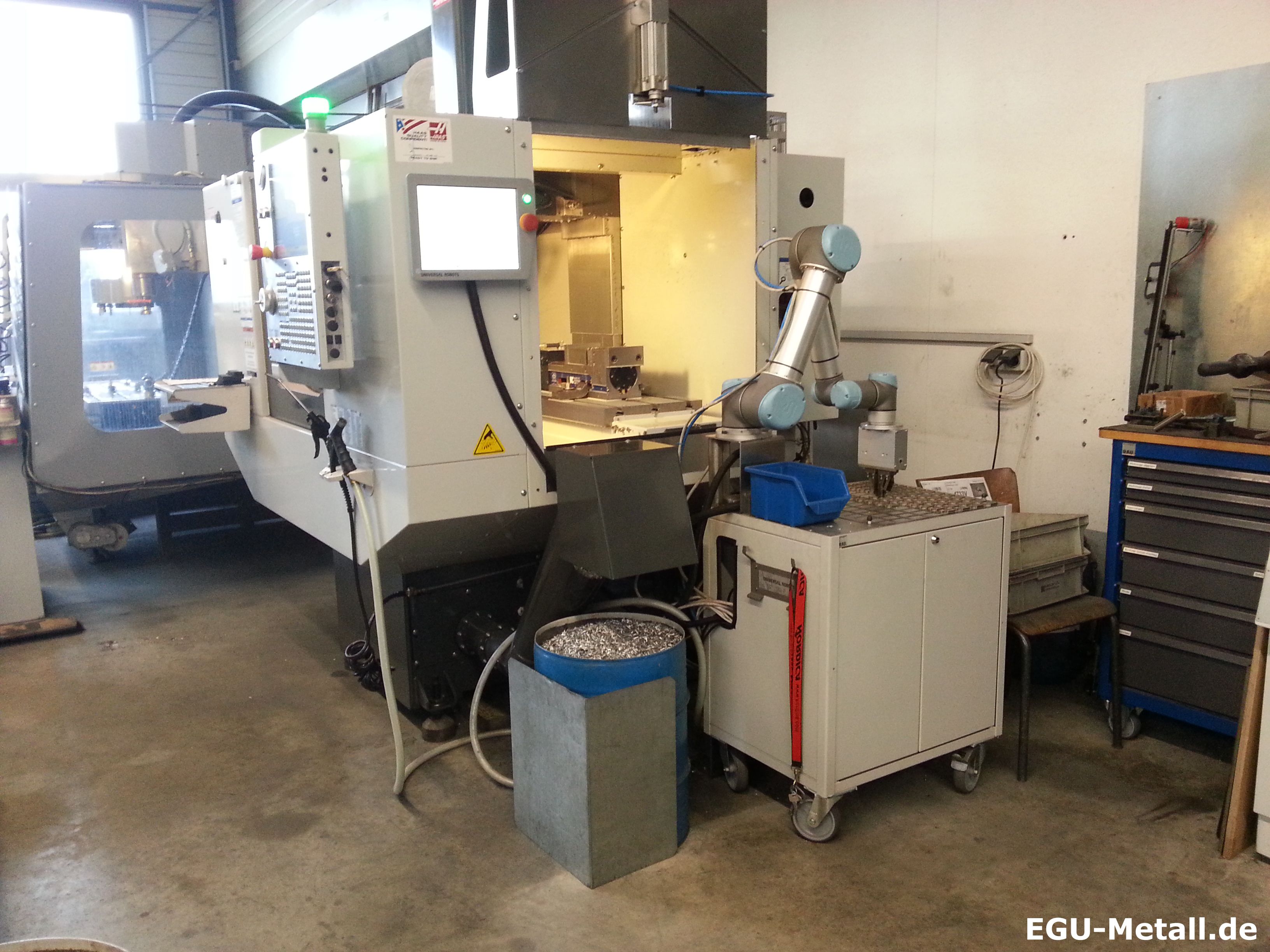 CNC machining centre with control panel beside a small industrial robot used for loading and unloading in a machine shop.