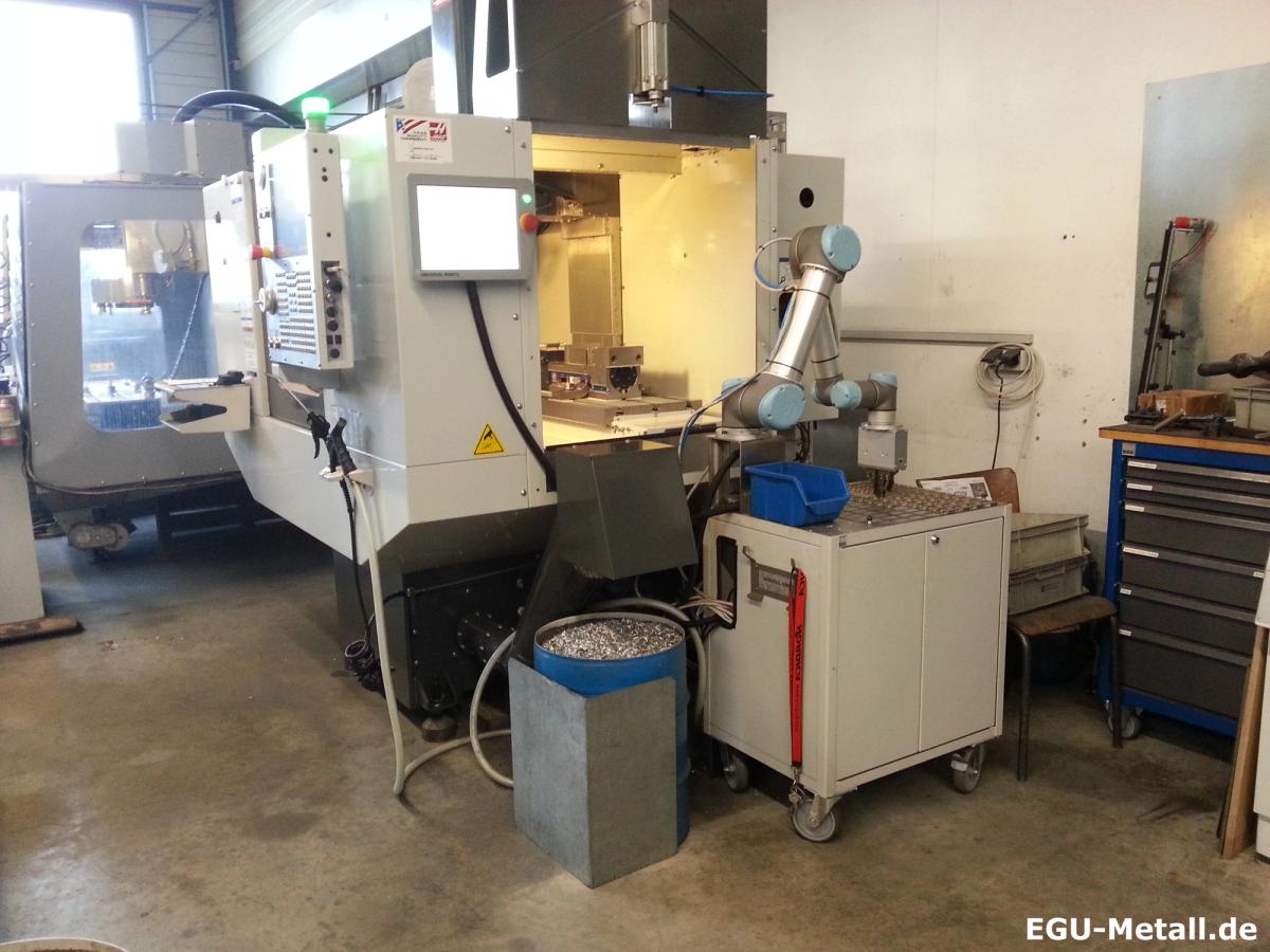 CNC machining centre with control panel beside a small industrial robot used for loading and unloading in a machine shop.