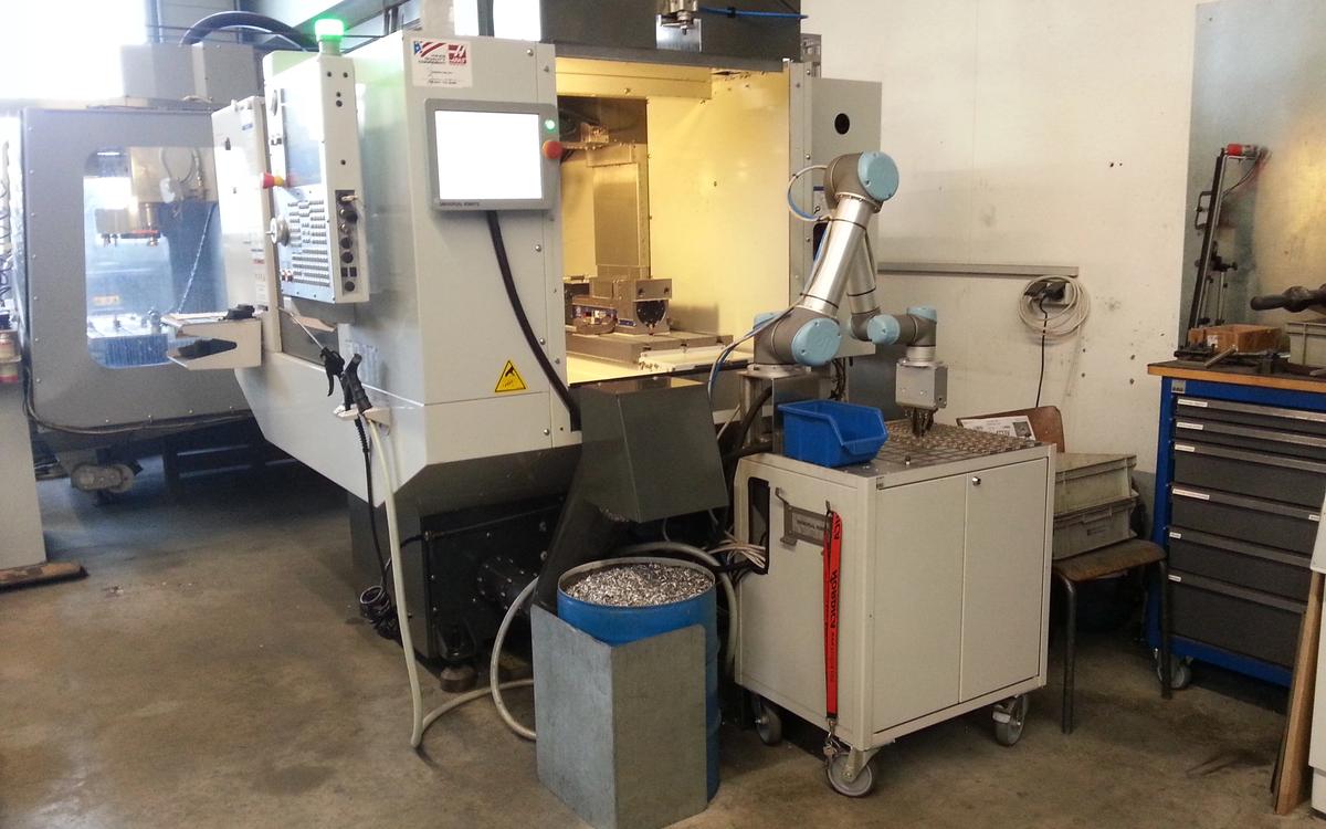 CNC machining centre with control panel beside a small industrial robot used for loading and unloading in a machine shop.