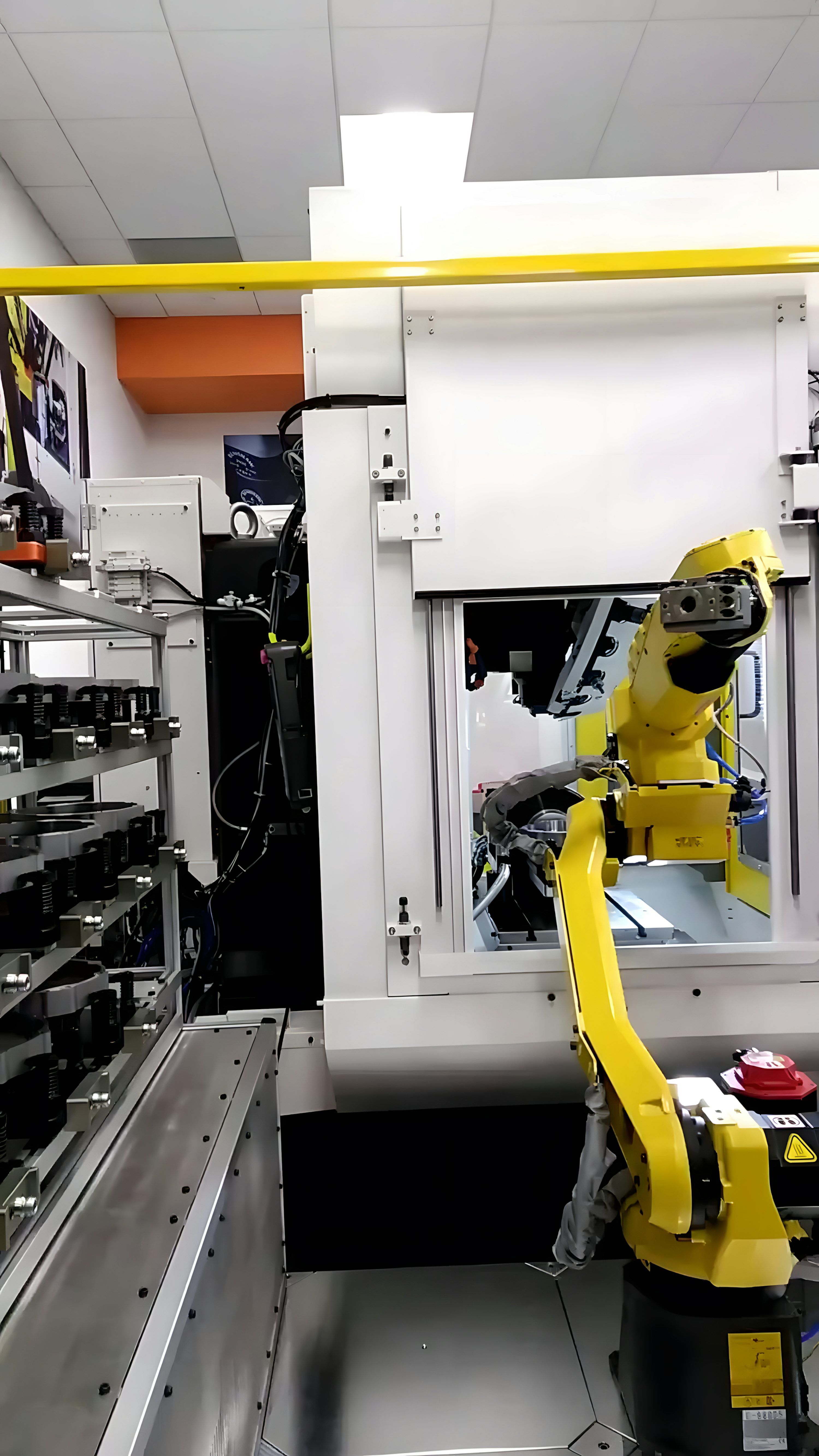 Yellow industrial robotic arm reaching toward the open enclosure of a CNC machine, with a rack of fixtures or tools on the left.
