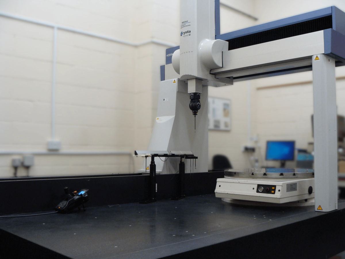 Five-axis scanning coordinate measuring machine with a vertical measurement head and rotary table in an inspection room.