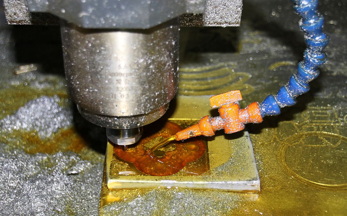 Close-up of a CNC milling spindle above a metal workpiece, with a flexible coolant nozzle directed at the cutting area.