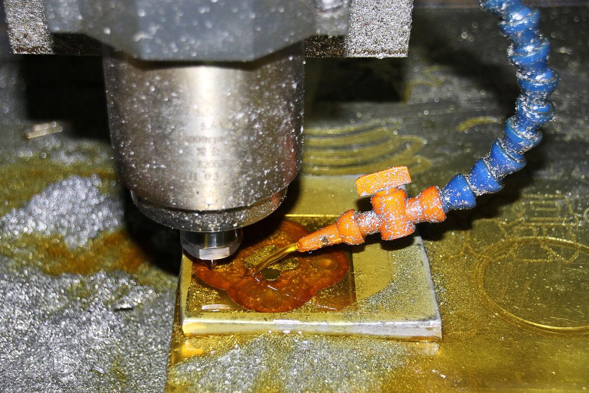 Close-up of a CNC milling spindle above a metal workpiece, with a flexible coolant nozzle directed at the cutting area.
