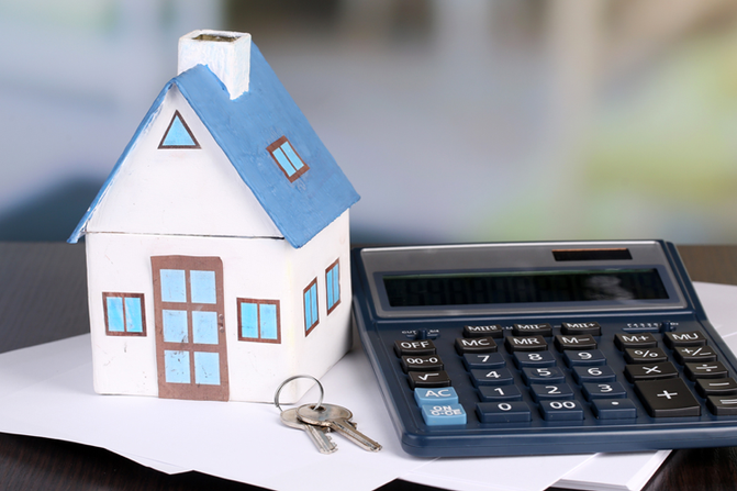 A calculator and a pair of keys next to a small white and blue model of a house