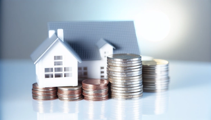 A white model house on top of a steady stack of coins