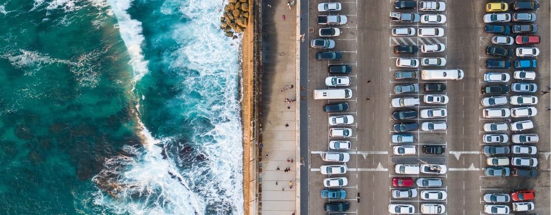 Overhead view of ocean waves crashing against a parking log of cars