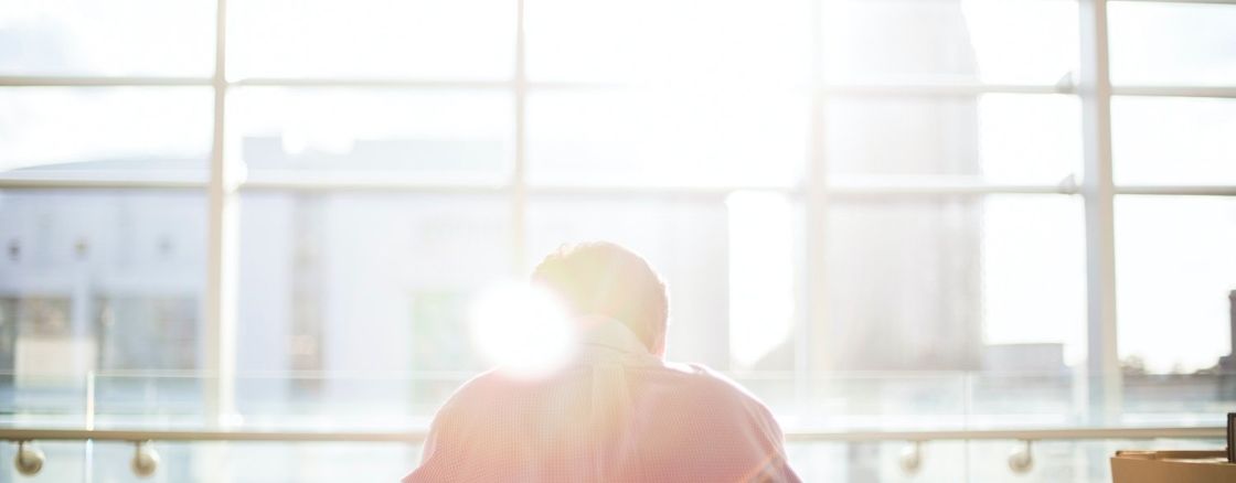 Person sitting at a desk facing a window while a lens flare obscures the foreground