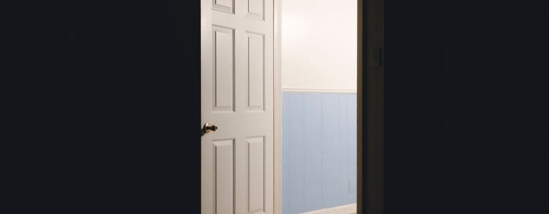 An open door in a dark room leading to a lit hallway