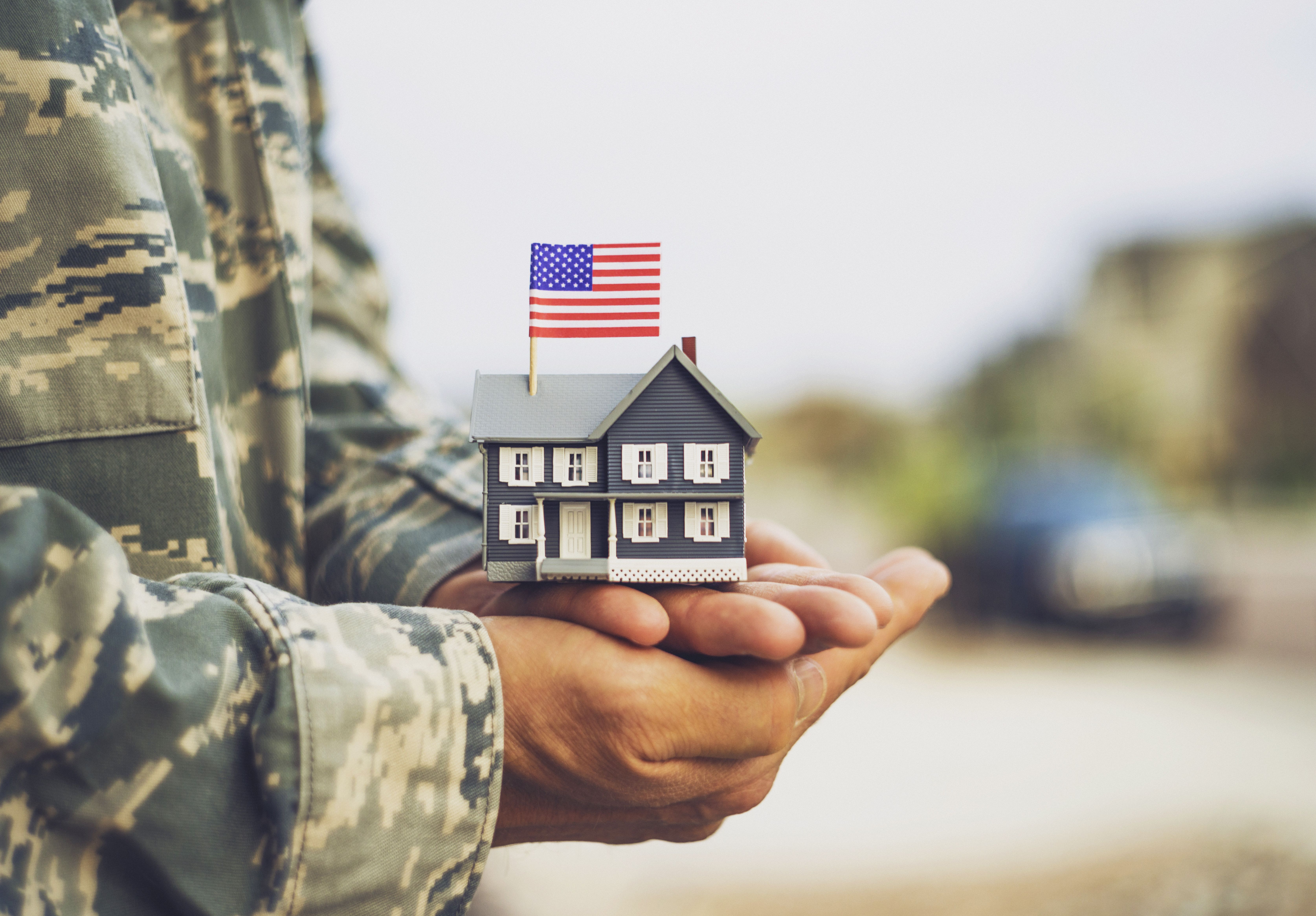 A veteran holds a home model with an American flag over his palm