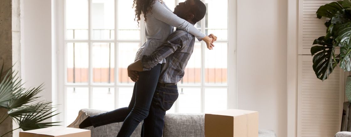 A man lifting up a women inside a room with packing boxes