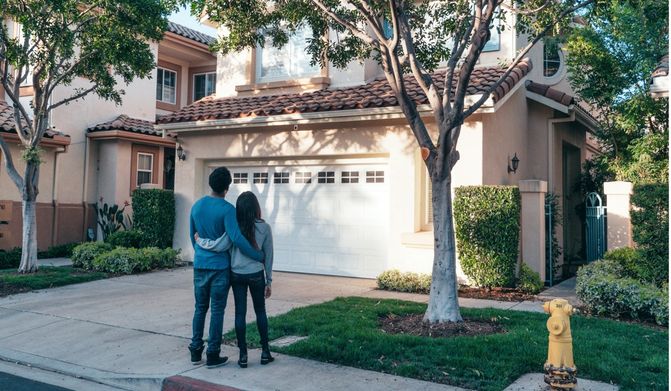 A couple with arms wrapped around each other and staring at a house