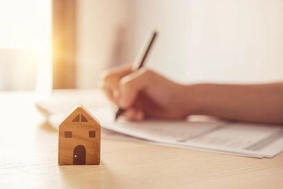 A hand writing on a document next to a tiny wooden toy house